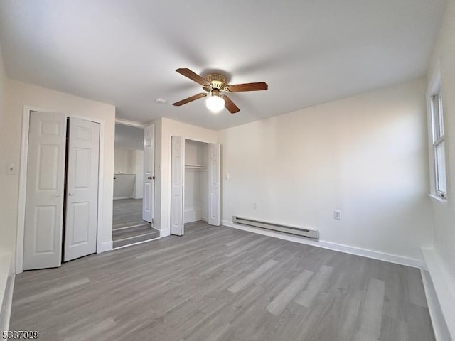 unfurnished bedroom with two closets, light hardwood / wood-style flooring, ceiling fan, and baseboard heating