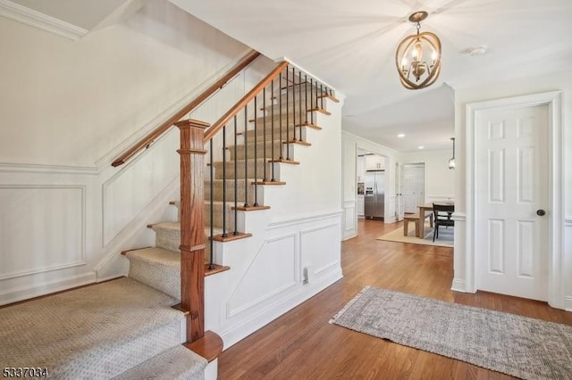 stairs featuring hardwood / wood-style flooring, ornamental molding, and an inviting chandelier