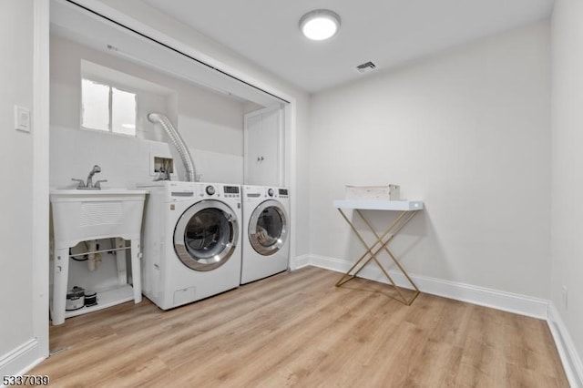 clothes washing area with washing machine and dryer and light wood-type flooring