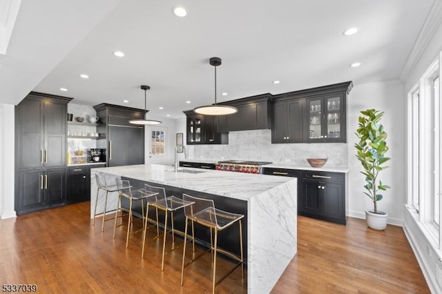 kitchen with a large island, a breakfast bar, light stone counters, decorative light fixtures, and wall chimney exhaust hood