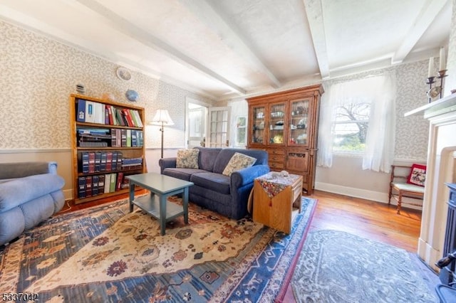 living room with a wainscoted wall, beam ceiling, and wallpapered walls