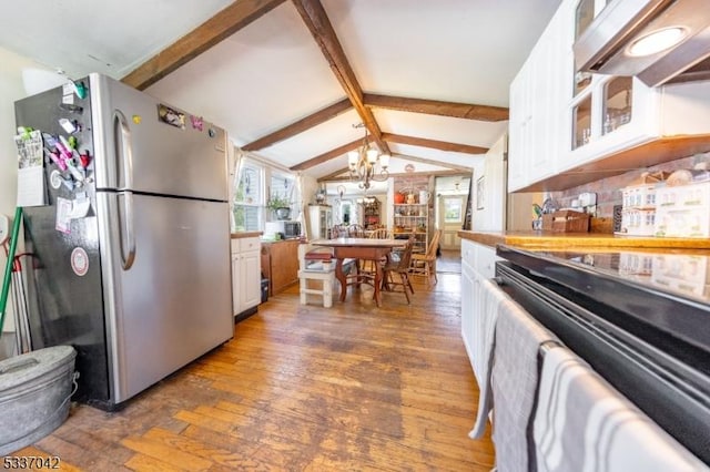 kitchen with white cabinets, lofted ceiling with beams, stove, hardwood / wood-style floors, and freestanding refrigerator