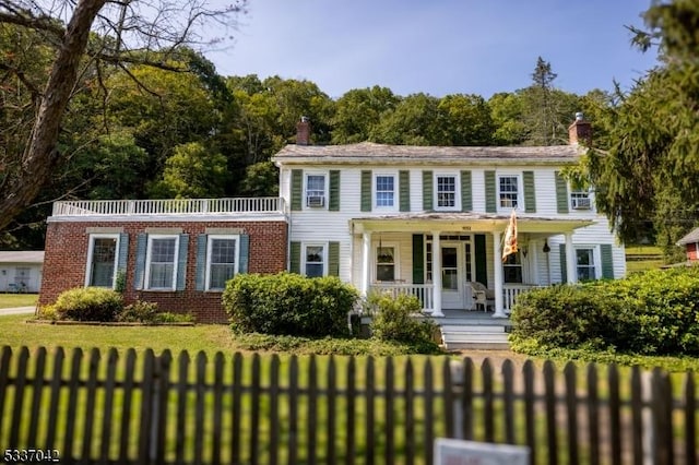 colonial-style house with a fenced front yard, brick siding, a chimney, covered porch, and a front lawn