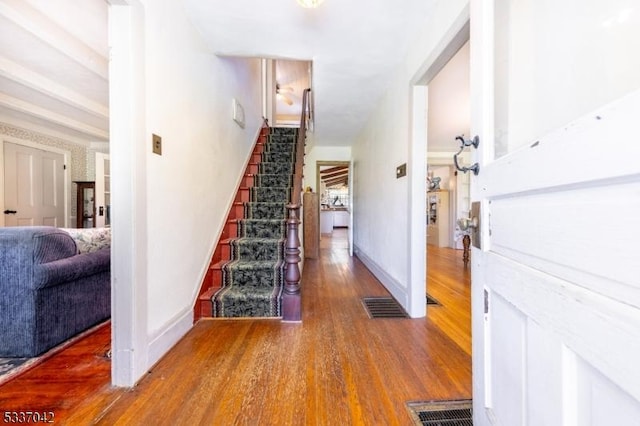 hallway featuring stairway, wood finished floors, visible vents, and baseboards