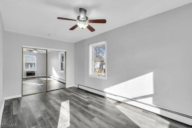 unfurnished bedroom with baseboard heating, ceiling fan, dark hardwood / wood-style flooring, and a closet