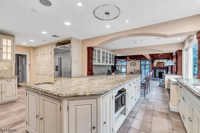 kitchen featuring sink, built in appliances, a center island with sink, a fireplace, and backsplash