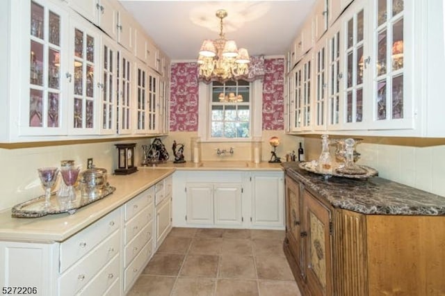 kitchen with sink, white cabinetry, a chandelier, hanging light fixtures, and dark stone counters