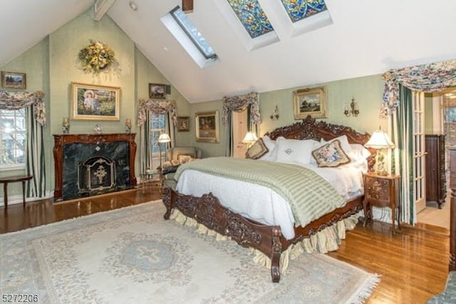 bedroom featuring a skylight, high vaulted ceiling, hardwood / wood-style flooring, a high end fireplace, and beam ceiling