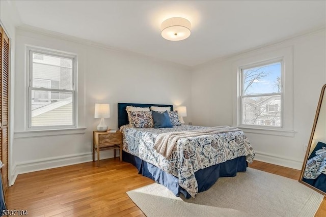 bedroom with a closet, crown molding, baseboards, and wood finished floors