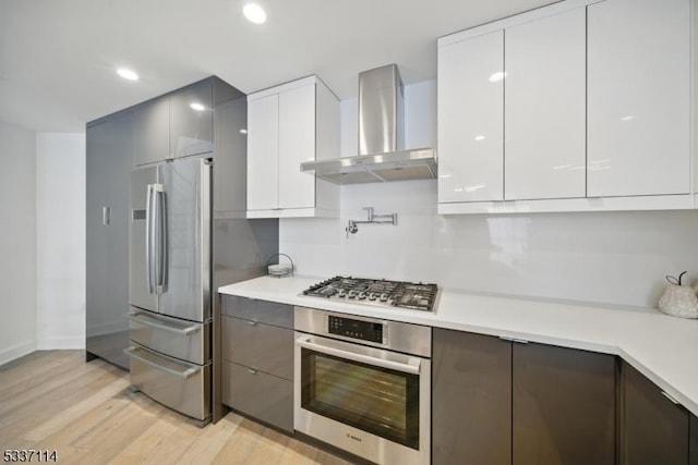 kitchen featuring white cabinetry, light hardwood / wood-style floors, stainless steel appliances, and wall chimney exhaust hood