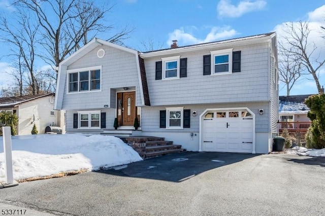 split foyer home featuring a garage, a chimney, and aphalt driveway