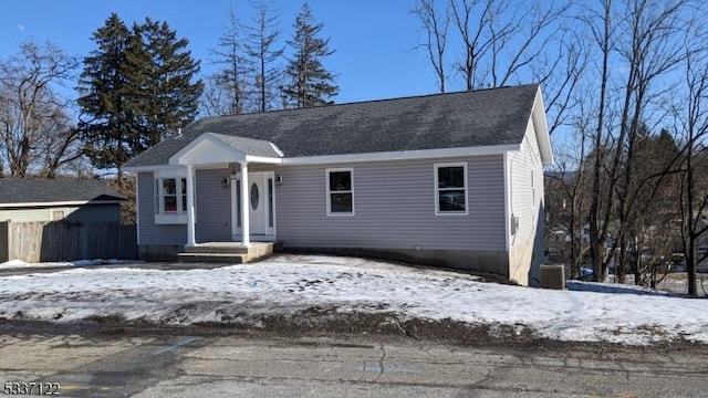 bungalow-style house featuring central AC unit, roof with shingles, and fence