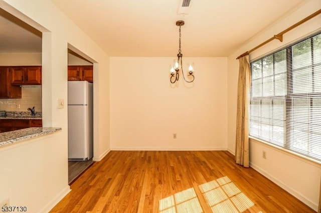 unfurnished dining area with sink, a notable chandelier, and light hardwood / wood-style floors