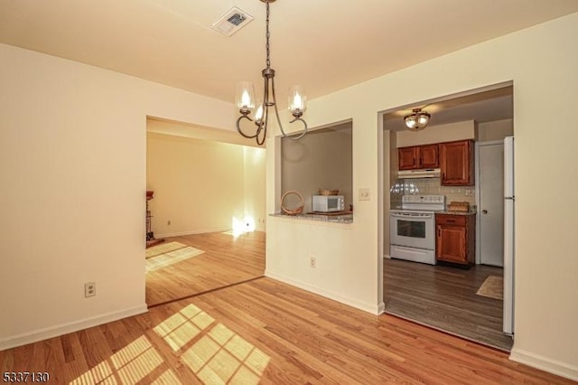 unfurnished dining area featuring a chandelier and light wood-type flooring