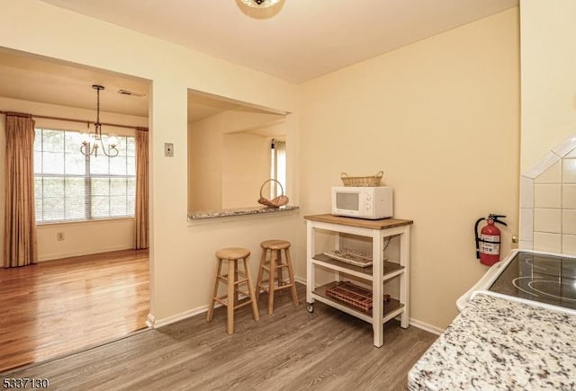 kitchen with an inviting chandelier, wood-type flooring, hanging light fixtures, light stone countertops, and stove