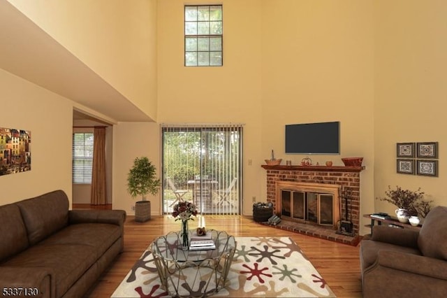 living room with a brick fireplace, hardwood / wood-style flooring, and a high ceiling