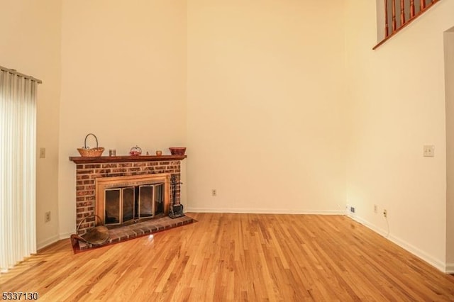 unfurnished living room with a brick fireplace, hardwood / wood-style flooring, and a towering ceiling