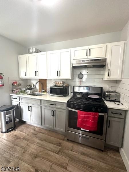 kitchen with stainless steel gas range oven, sink, dark wood-type flooring, and white cabinets