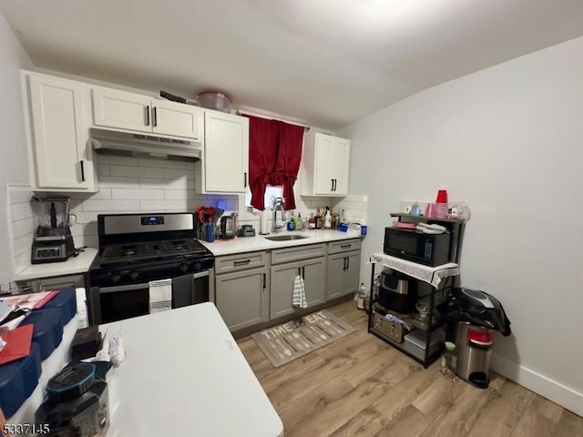 kitchen with sink, stainless steel range with gas stovetop, light hardwood / wood-style floors, white cabinets, and decorative backsplash