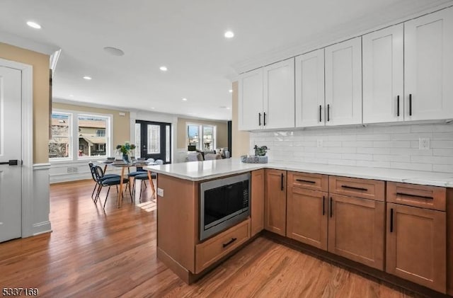 kitchen with stainless steel microwave, white cabinetry, decorative backsplash, kitchen peninsula, and light wood-type flooring