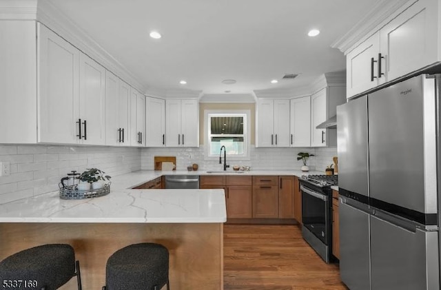 kitchen featuring appliances with stainless steel finishes, white cabinetry, sink, light stone counters, and kitchen peninsula