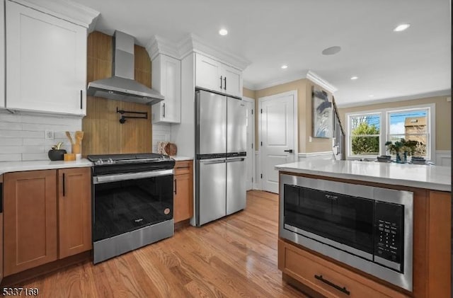 kitchen featuring light hardwood / wood-style flooring, appliances with stainless steel finishes, white cabinetry, tasteful backsplash, and wall chimney exhaust hood