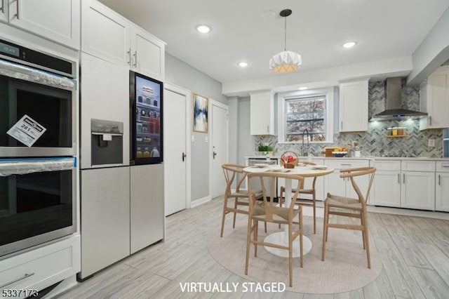 kitchen featuring stainless steel appliances, wall chimney range hood, white cabinets, and backsplash