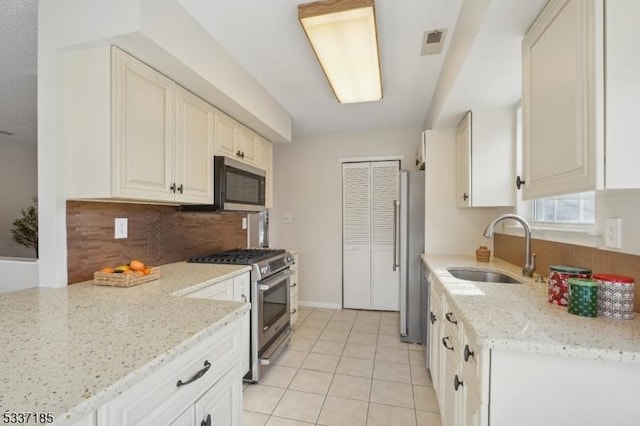 kitchen featuring visible vents, a sink, stainless steel appliances, decorative backsplash, and light stone countertops