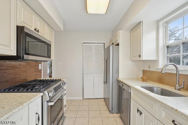 kitchen with light stone counters, light tile patterned flooring, a sink, decorative backsplash, and stainless steel appliances