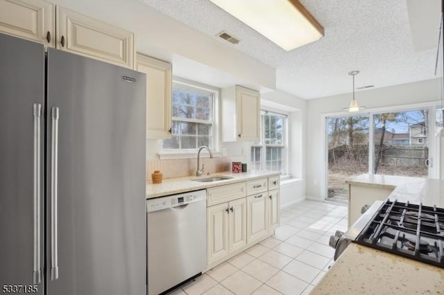 kitchen featuring visible vents, cream cabinetry, high end fridge, a sink, and dishwashing machine