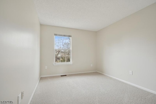 spare room featuring carpet flooring, baseboards, visible vents, and a textured ceiling