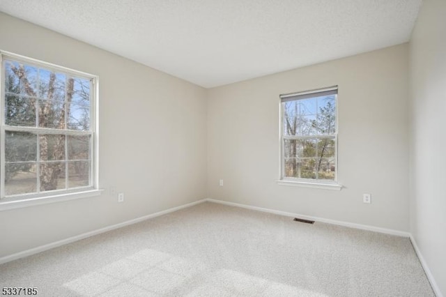 carpeted spare room featuring baseboards, visible vents, and a textured ceiling