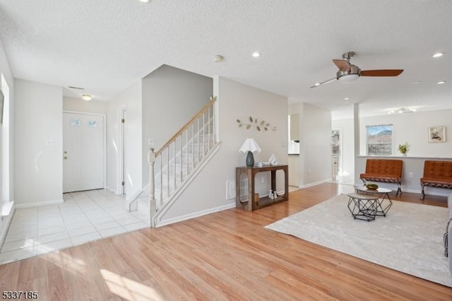 living area with stairway, a ceiling fan, wood finished floors, baseboards, and a textured ceiling