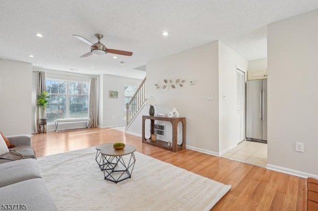 living area with light wood-type flooring, recessed lighting, stairway, baseboards, and ceiling fan