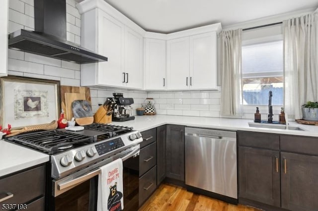 kitchen featuring white cabinetry, sink, light hardwood / wood-style floors, stainless steel appliances, and wall chimney exhaust hood