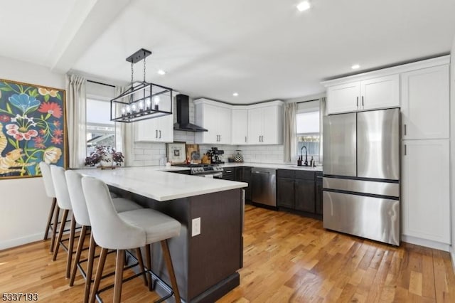 kitchen featuring wall chimney exhaust hood, sink, white cabinetry, hanging light fixtures, and stainless steel appliances