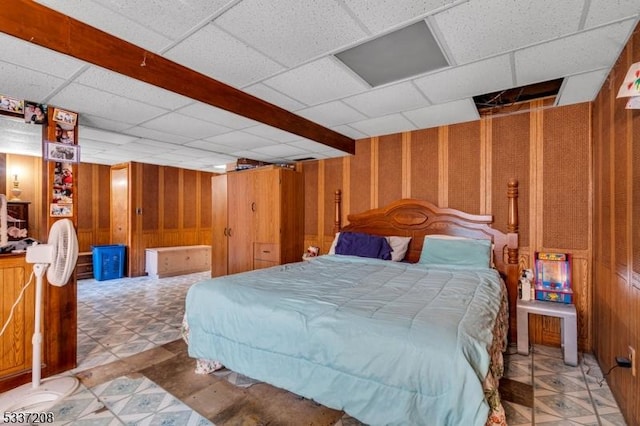 bedroom featuring a drop ceiling, light floors, and wooden walls