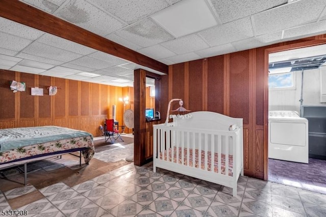 bedroom with a drop ceiling, light floors, washer / clothes dryer, and wood walls