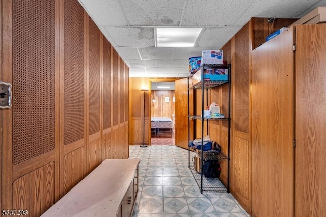 hall with a paneled ceiling, light floors, and wooden walls