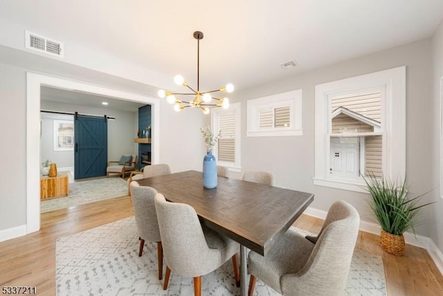 dining space with a notable chandelier, light hardwood / wood-style floors, and a barn door