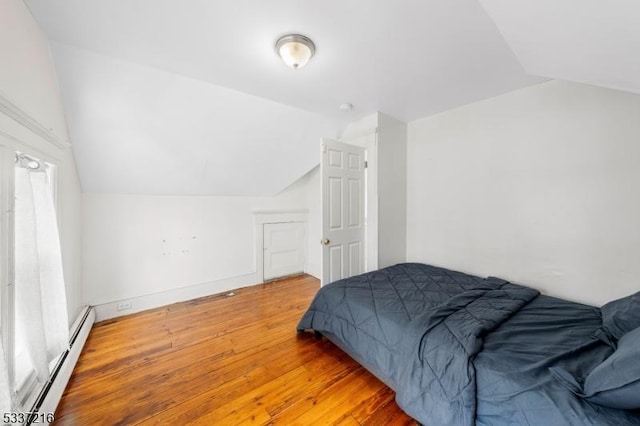 bedroom featuring wood-type flooring, vaulted ceiling, and a baseboard heating unit