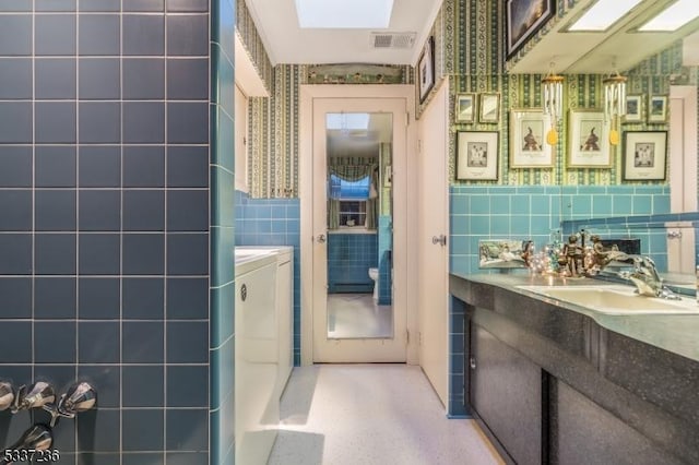 bathroom with washing machine and dryer, tile walls, vanity, and a skylight