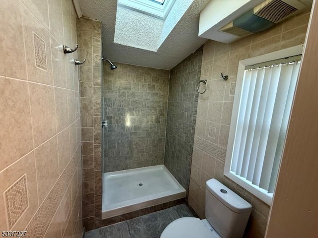 bathroom with a skylight, tile walls, tiled shower, toilet, and a textured ceiling