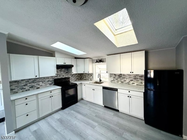 kitchen featuring sink, white cabinetry, light hardwood / wood-style flooring, vaulted ceiling with skylight, and black appliances