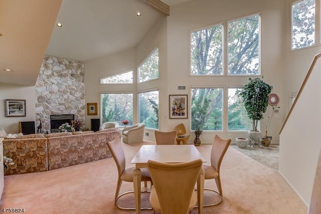 carpeted dining area with a stone fireplace and a high ceiling