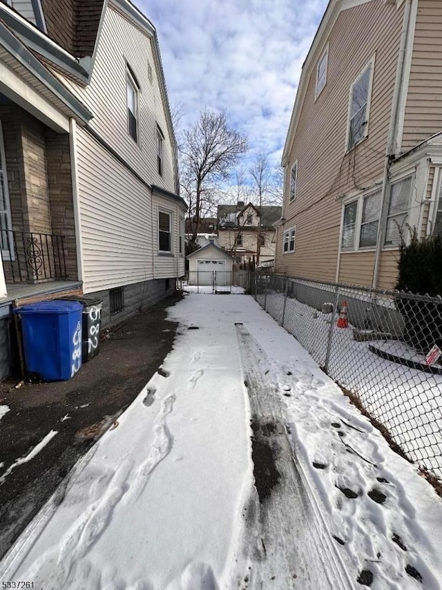 view of snowy exterior featuring a detached garage, driveway, and fence