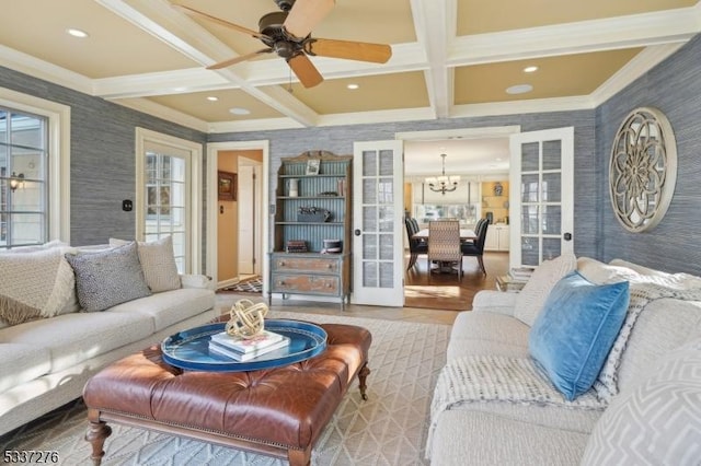 living room with coffered ceiling, ceiling fan with notable chandelier, ornamental molding, and french doors