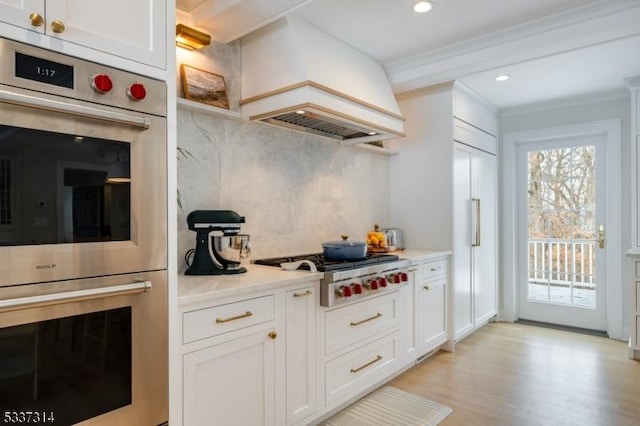 kitchen featuring premium range hood, white cabinetry, stainless steel appliances, and backsplash