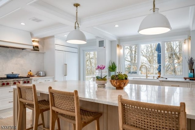 kitchen with paneled built in refrigerator, decorative light fixtures, a kitchen bar, and white cabinets