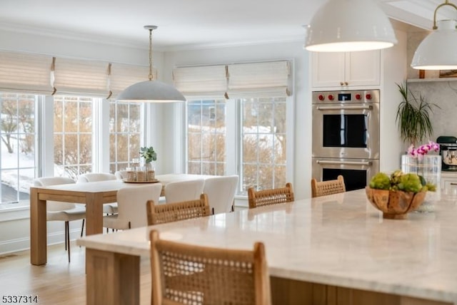 kitchen with crown molding, plenty of natural light, double oven, and hanging light fixtures